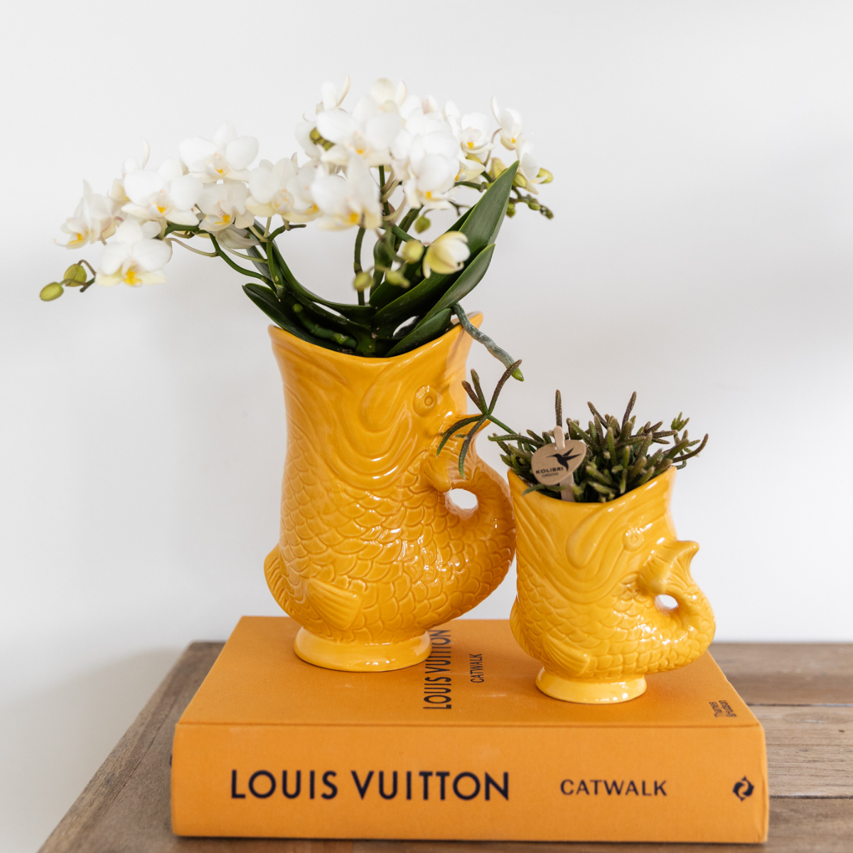 Everspring gele keramische visvormige plantenpotten met witte orchidee en groene plant op Louis Vuitton boek